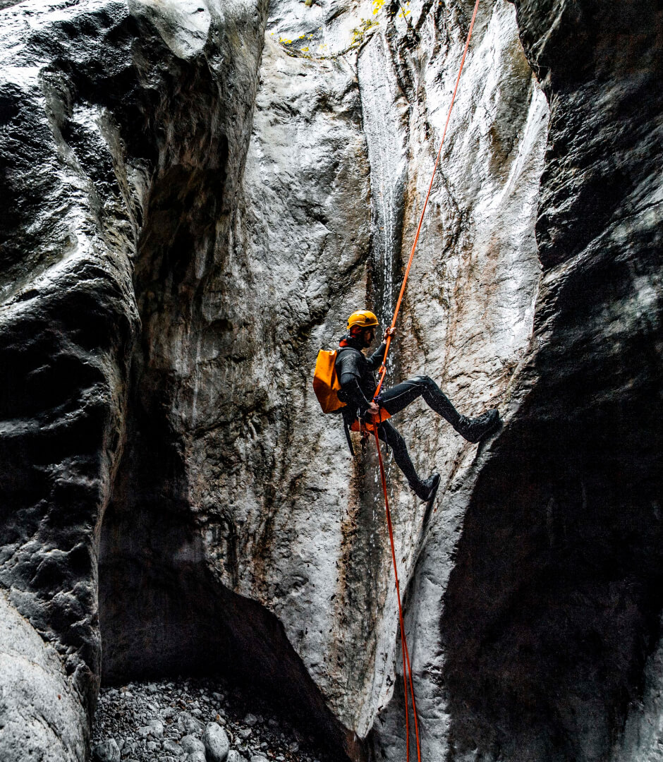 A canyoneering male making an abseil down the static rope into a dark stone cave content-image